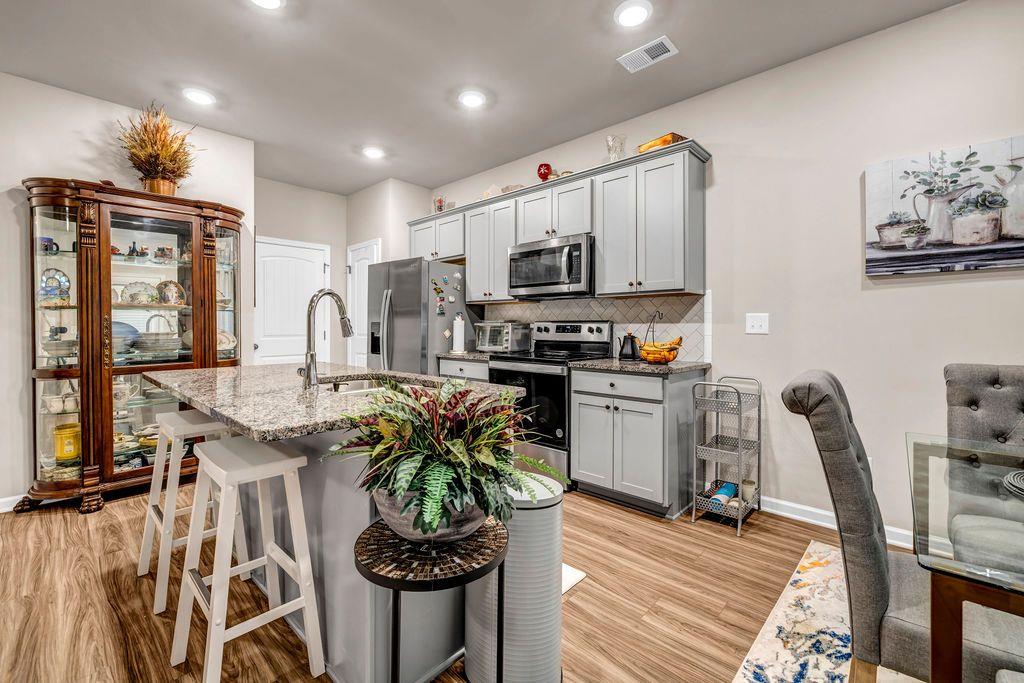 255 Skipjack Court Covington, GA 30016 - Photo 9 of 24 a kitchen with stainless steel appliances kitchen island granite countertop a stove top oven a sink a dining table and chairs with wooden floor