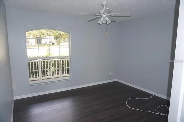 an empty room with wooden floor fan and windows