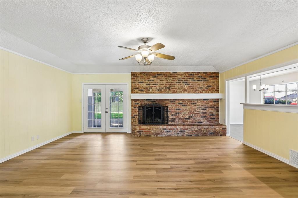 1600 South Timber Court Benbrook, TX 76126 - Photo 4 of 30 Spacious living area featuring wood-finish flooring, a brick fireplace with a white mantle, and a ceiling fan with light fixture