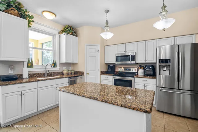 a kitchen with granite countertop a refrigerator a sink a stove and wooden cabinets