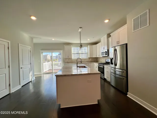 a kitchen with stainless steel appliances granite countertop a refrigerator a sink dishwasher a stove and white countertops with wooden floor