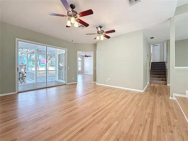 a view of an empty room with wooden floor and a ceiling fan