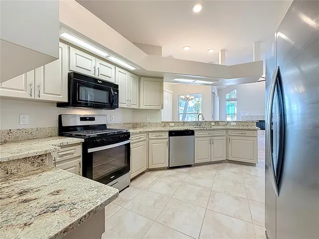 a kitchen with stainless steel appliances kitchen island granite countertop a stove top oven a sink dishwasher a refrigerator and a cabinets