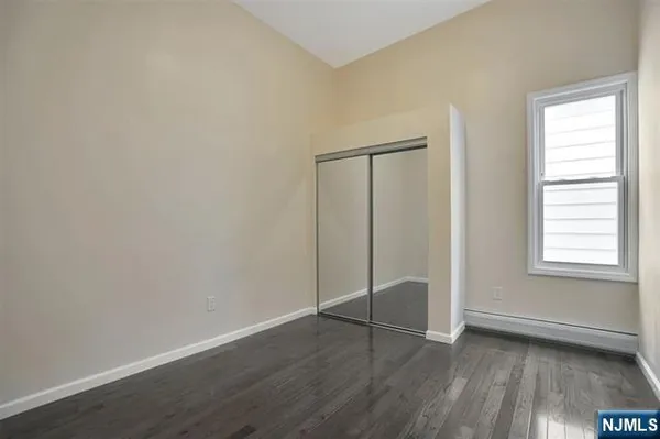 an empty room with wooden floor closet and windows