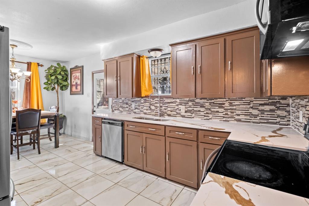 2133 Pleasant Drive Dallas, TX 75227 - Photo 11 of 40 Kitchen featuring extractor fan, brown cabinets, appliances with stainless steel finishes, light marble finish flooring, and light stone countertops