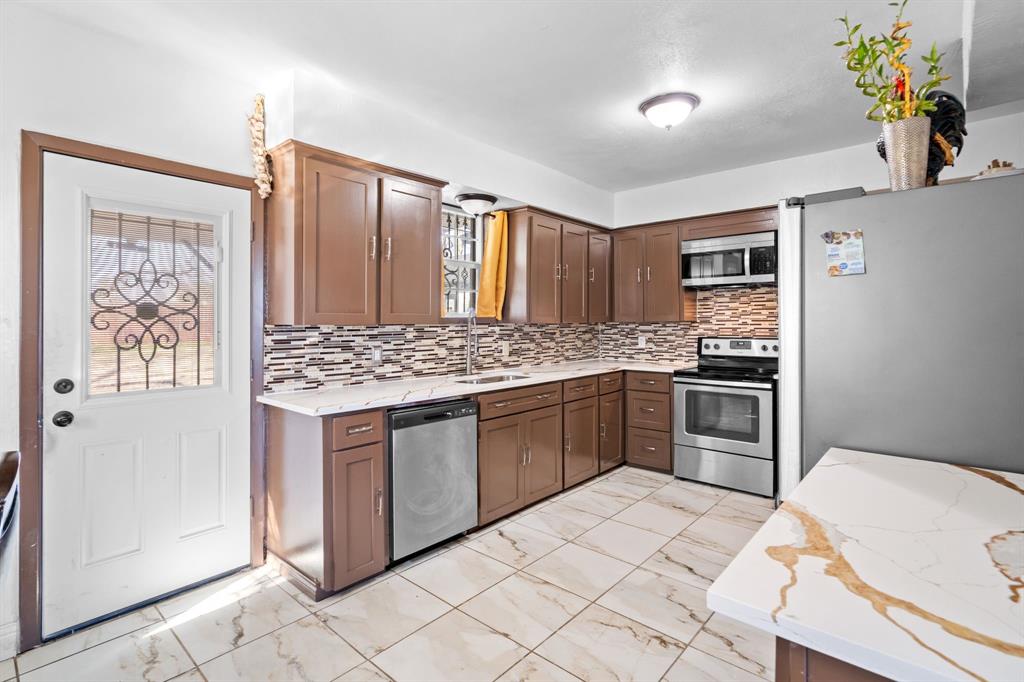 2133 Pleasant Drive Dallas, TX 75227 - Photo 12 of 40 Kitchen featuring appliances with stainless steel finishes, light stone counters, light marble finish floors, tasteful backsplash, and dark brown cabinetry