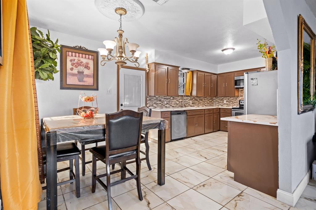 2133 Pleasant Drive Dallas, TX 75227 - Photo 9 of 40 Kitchen with brown cabinetry, appliances with stainless steel finishes, hanging light fixtures, a chandelier, and backsplash