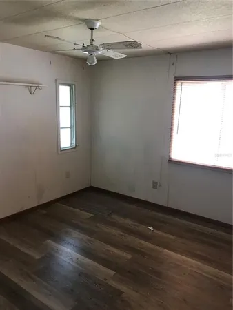 an empty room with wooden floor ceiling fan and windows