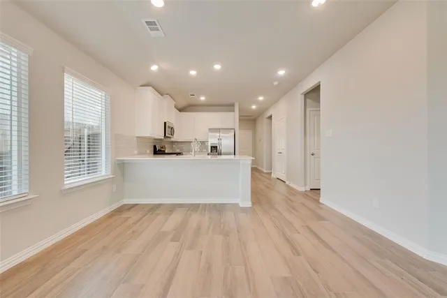 a large white kitchen with kitchen island a sink wooden floor and a refrigerator