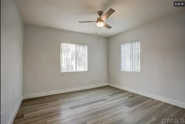 an empty room with wooden floor ceiling fan and windows