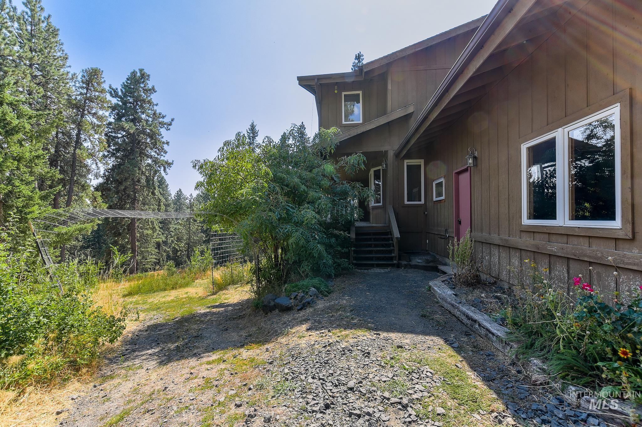 1045 Joyce Road Moscow, ID 83843 - Photo 46 of 50 Wood-sided exterior with white-framed windows, a red entry door, and a gravel pathway