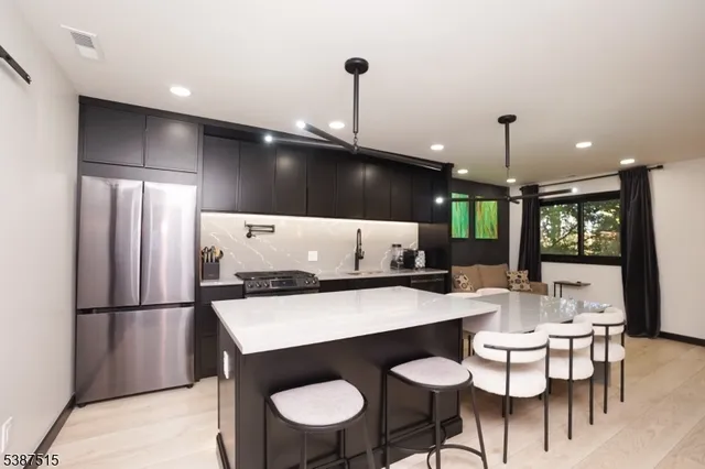 a kitchen with stainless steel appliances kitchen island granite countertop a dining table chairs and a refrigerator