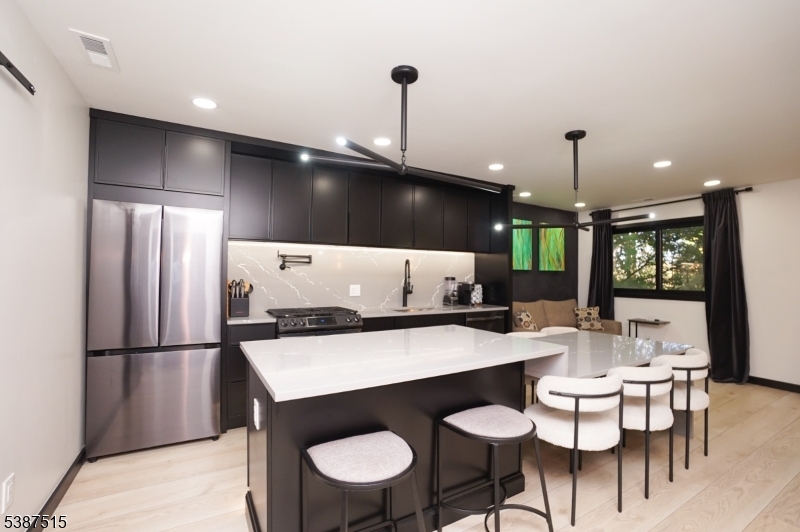 a kitchen with stainless steel appliances kitchen island granite countertop a dining table chairs and a refrigerator