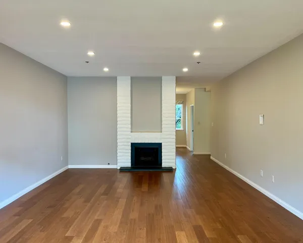 an empty room with wooden floor fireplace and windows