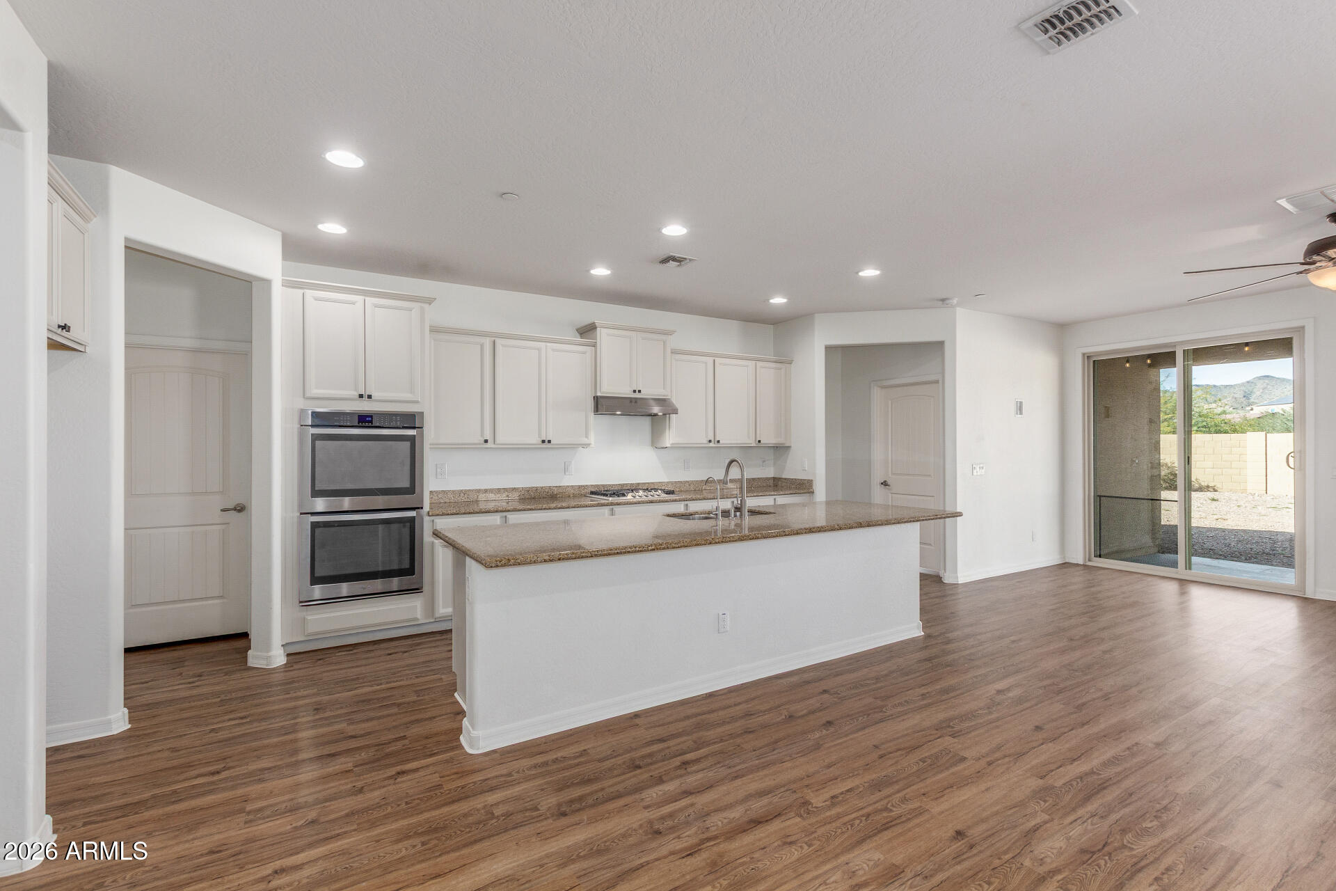 21294 West Berkeley Road Buckeye, AZ 85396 - Photo 7 of 34 a large kitchen with kitchen island a sink a stove a refrigerator and white cabinets with wooden floor