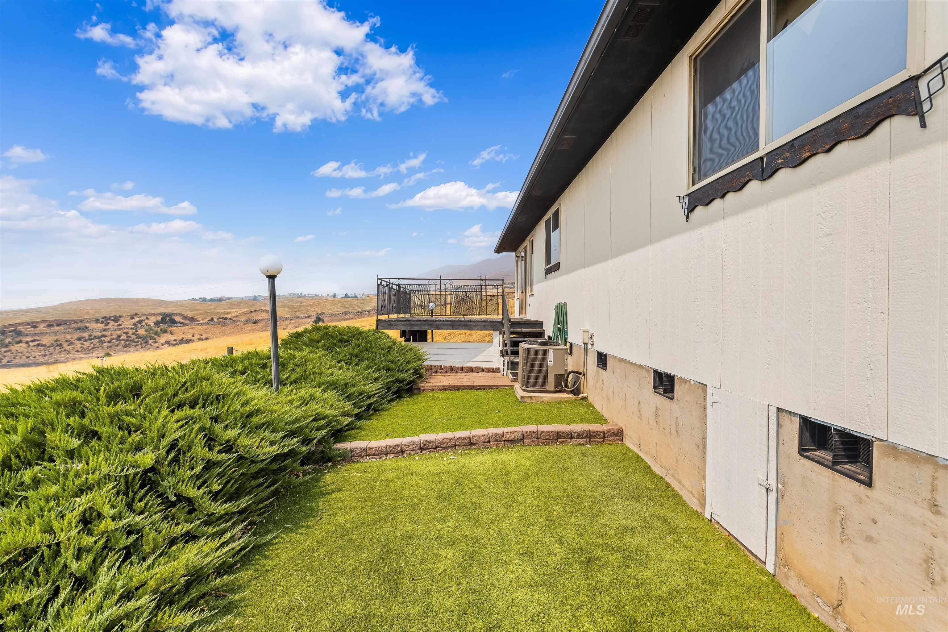 1133 Harvest Road Lewiston, ID 83501 - Photo 13 of 45 Exterior featuring an elevated wood deck with metal railing, white siding, and a partially exposed concrete foundation with small windows