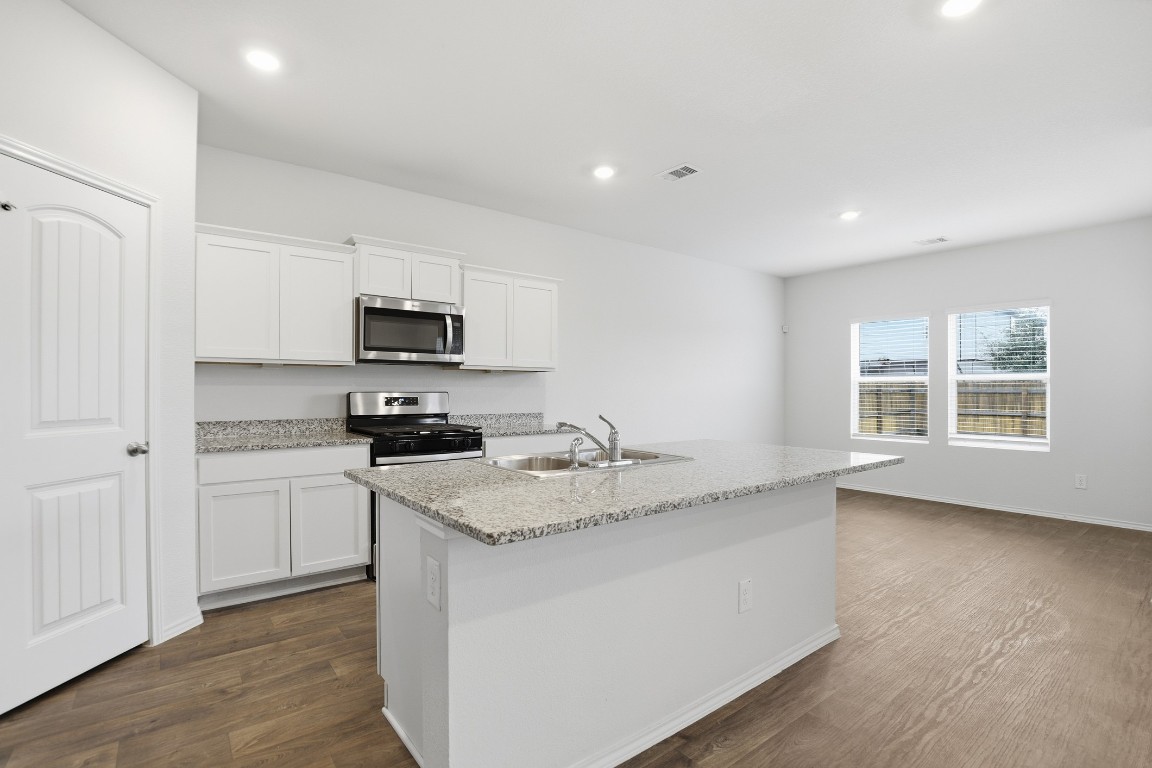 427 Sickle Loop Kyle, TX 78640 - Photo 25 of 39 Kitchen featuring appliances with stainless steel finishes, white cabinets, dark wood-style floors, an island with sink, and light stone countertops