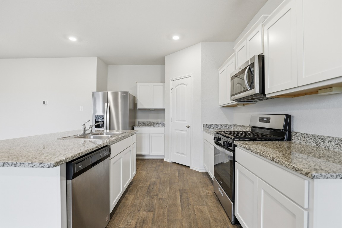 427 Sickle Loop Kyle, TX 78640 - Photo 27 of 39 Kitchen with appliances with stainless steel finishes, dark wood-style flooring, an island with sink, white cabinetry, and light stone counters