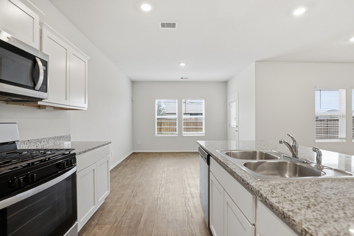 427 Sickle Loop Kyle, TX 78640 - Photo 29 of 39 Kitchen featuring stainless steel appliances, white cabinetry, light wood-style floors, recessed lighting, and light stone countertops