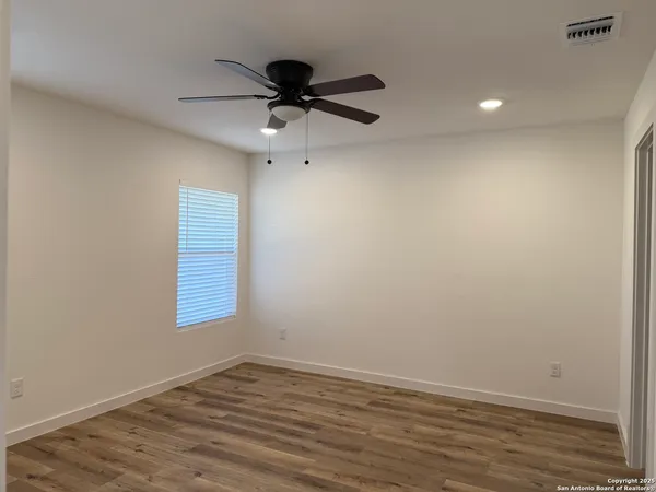 an empty room with wooden floor fan and windows
