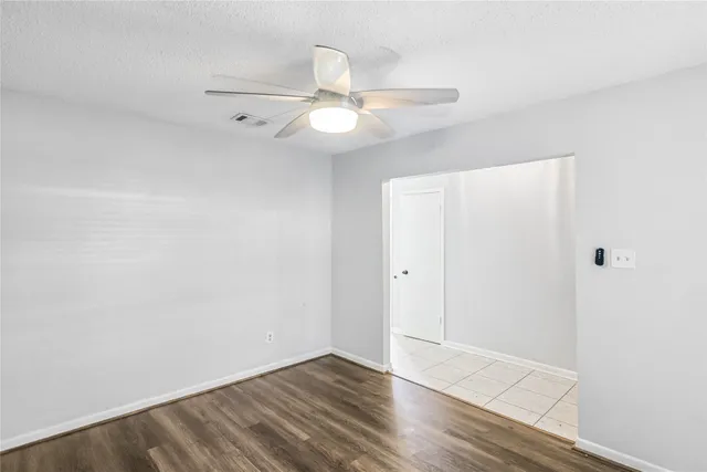 an empty room with wooden floor fan and windows