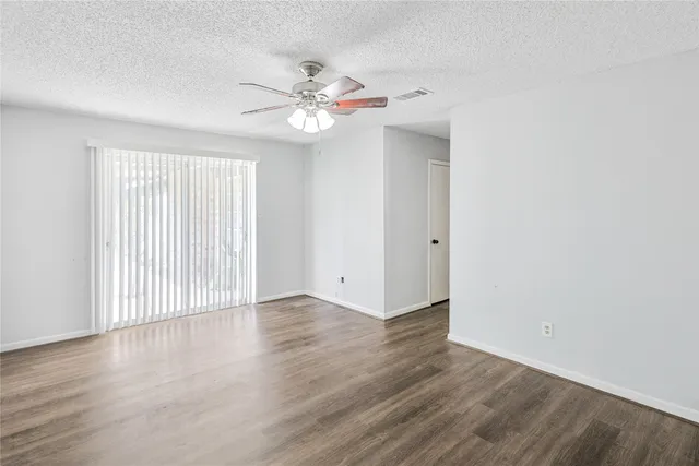 an empty room with wooden floor fan and windows