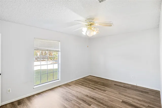 an empty room with wooden floor fan and window