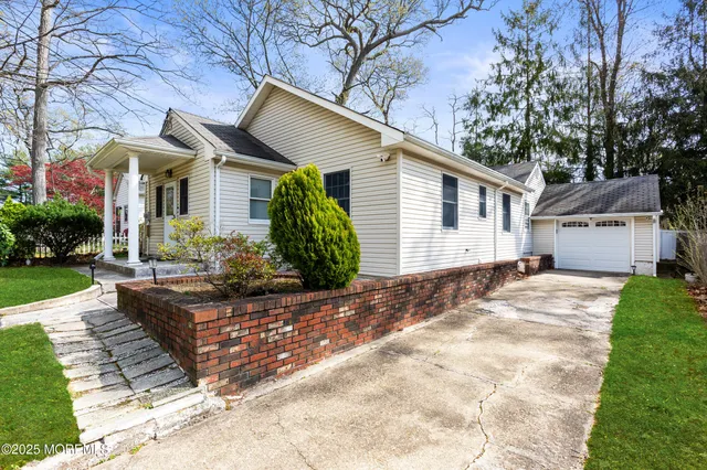 a view of a white house next to a yard with potted plants and large trees
