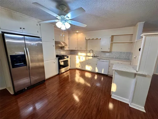 a kitchen with stainless steel appliances a refrigerator a sink dishwasher a stove and white cabinets with wooden floor