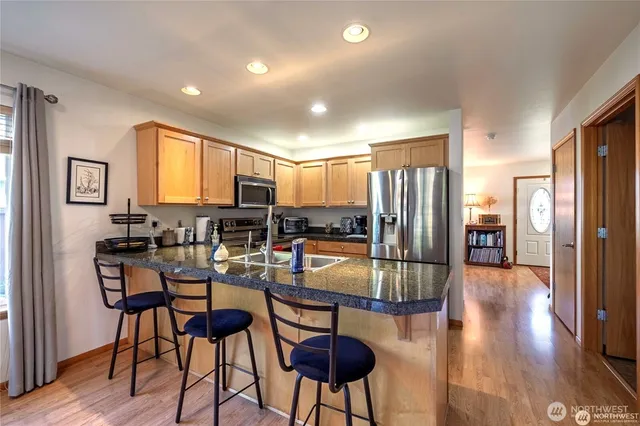 a kitchen with stainless steel appliances granite countertop a refrigerator a stove a sink a dining table and chairs with wooden floor