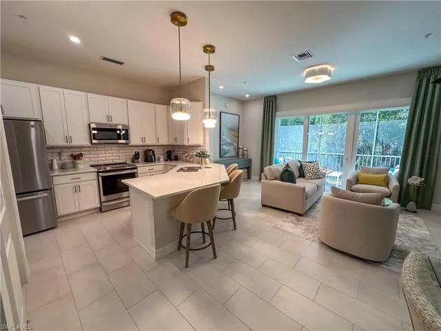 a kitchen with stainless steel appliances kitchen island granite countertop a refrigerator a stove a sink a dining table and chairs with the floor
