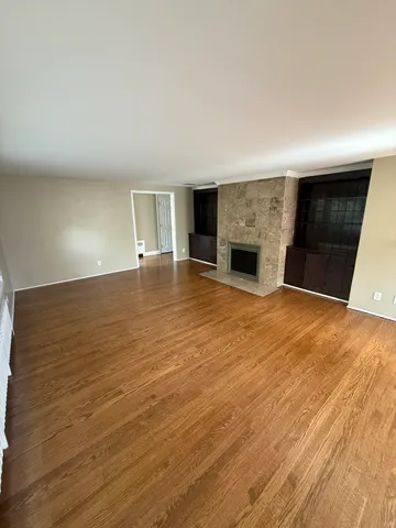 an empty room with wooden floor fireplace and windows