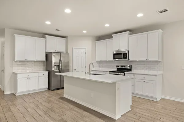 a kitchen with stainless steel appliances a sink stove refrigerator and white cabinets with wooden floor