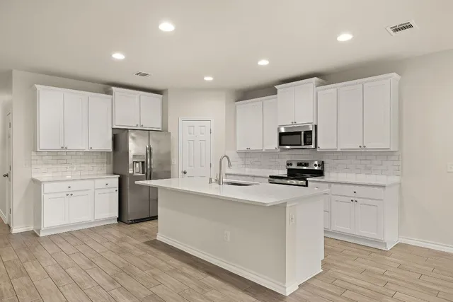 a kitchen with stainless steel appliances a sink stove refrigerator and white cabinets with wooden floor