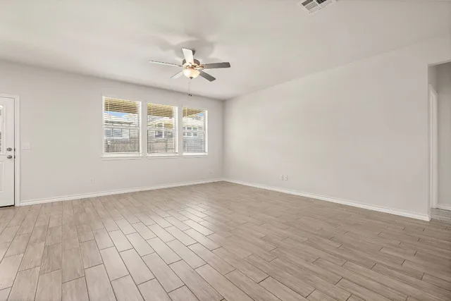 an empty room with wooden floor chandelier fan and windows