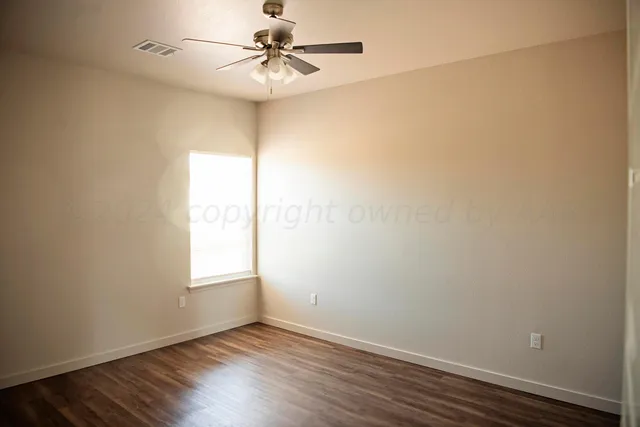 an empty room with wooden floor fan and windows
