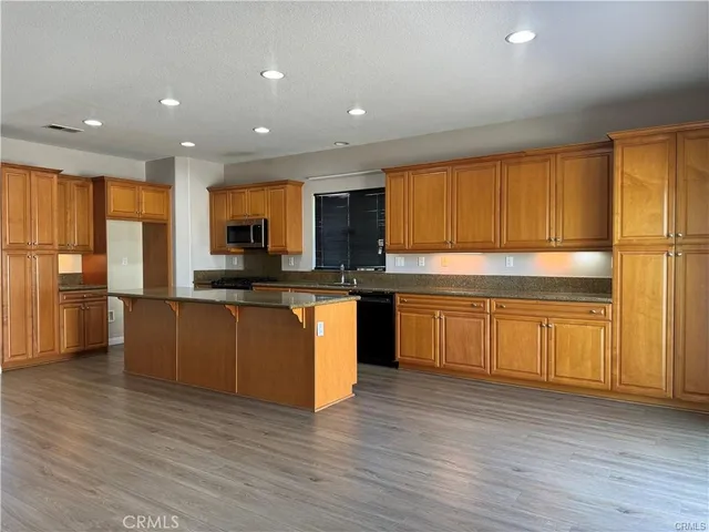a kitchen with granite countertop wooden floors stainless steel appliances and a window