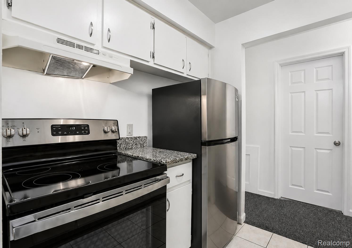 Stainless steel refrigerator, stainless steel electric range, granite-finish countertop, white cabinetry, and a white paneled door