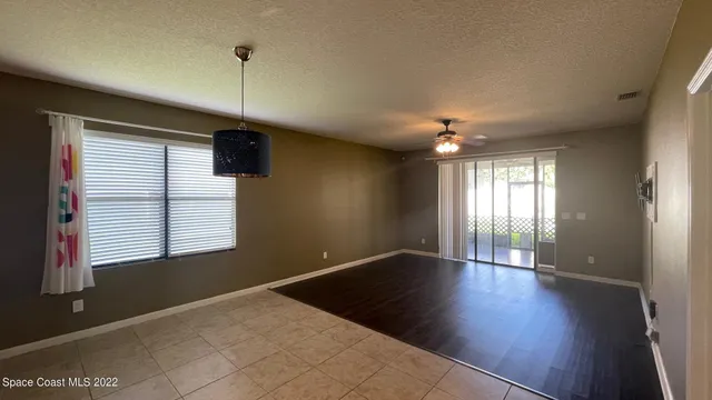 an empty room with wooden floor chandelier fan and windows