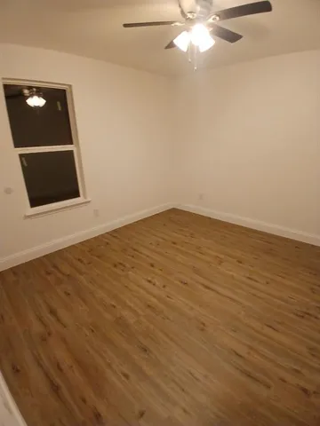 a view of an empty room with wooden floor and a ceiling fan