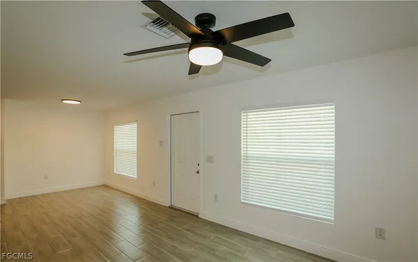 an empty room with wooden floor ceiling fan and windows