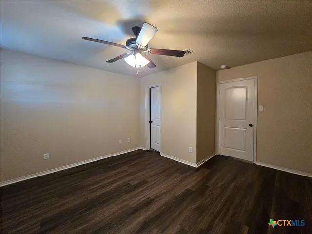 a view of an empty room with wooden floor and a ceiling fan