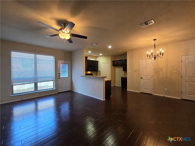 a view of an empty room with wooden floor and a kitchen