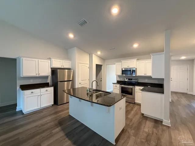 a kitchen with stainless steel appliances granite countertop a sink a stove a refrigerator and white cabinets with wooden floor