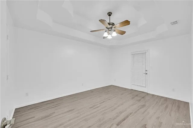 a view of an empty room with wooden floor and a ceiling fan