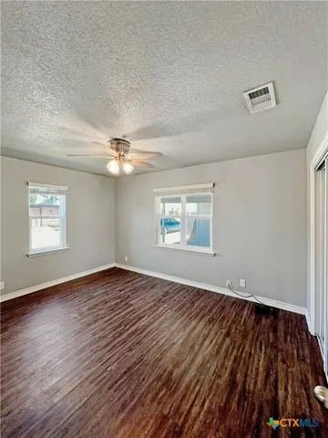 a view of an empty room with wooden floor and a ceiling fan