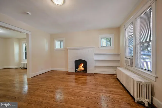 a view of an empty room with wooden floor fireplace and a window
