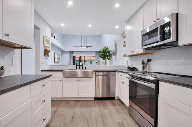 a kitchen with stainless steel appliances granite countertop white cabinets a sink a stove a microwave and wooden floors