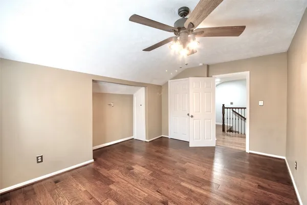 an empty room with wooden floor chandelier fan and windows