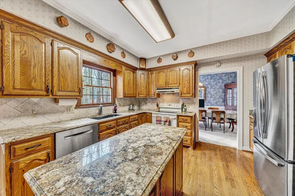 a kitchen with stainless steel appliances granite countertop a refrigerator a sink dishwasher a stove and white countertops with wooden floor